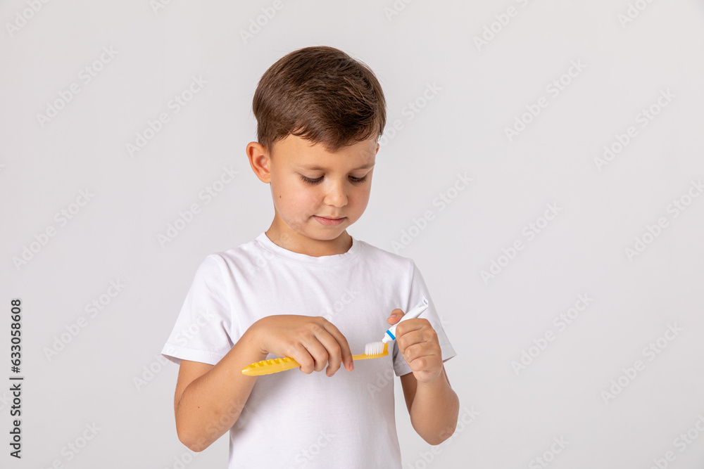 Morning concept. Close-up portrait of a happy little boy with toothbrush on white background. A child in a white T-shirt brushes his teeth on his own. Space for text Morning concept. Close-up portrait of a happy little boy with toothbrush on white background. A child in a white T-shirt brushes his teeth on his own. Space for text