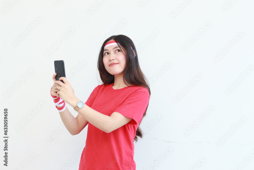 portrait of beautiful asian woman wearing red outfit celebrating Indonesia independence day holding mobile phone and smiling portrait of beautiful asian woman wearing red outfit celebrating Indonesia independence day holding mobile phone and smiling