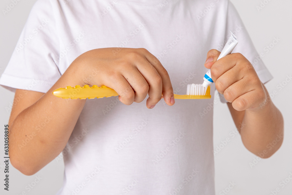 The child's hands squeeze the toothpaste onto the toothbrush. Morning concept. Close-up portrait of a happy little boy with toothbrush on white background. The child's hands squeeze the toothpaste onto the toothbrush. Morning concept. Close-up portrait of a happy little boy with toothbrush on white background.