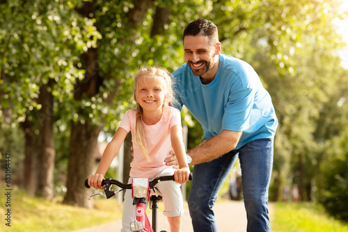 Loving middle aged father and his pretty daughter spending time together oudoors, dad teaching child how to ride a bike © Prostock-studio