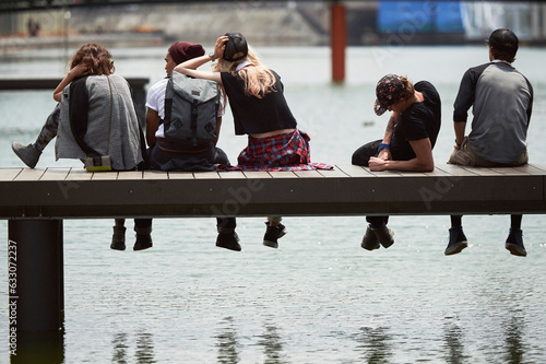 Teenage friends sitting on jetty over river photo