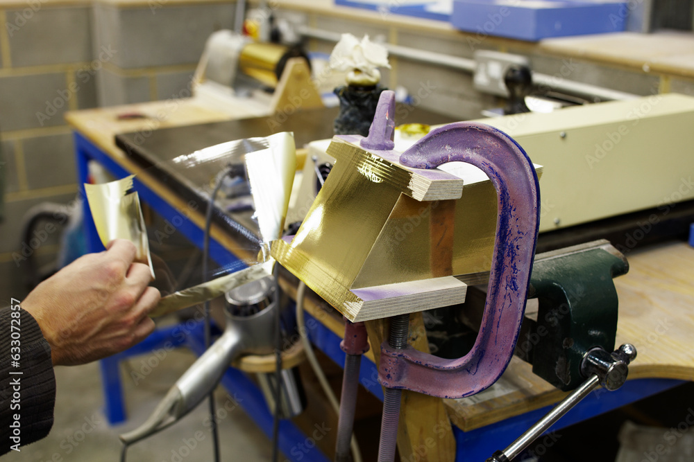 Hand of man applying gold foil to wood Hand of man applying gold foil to wood