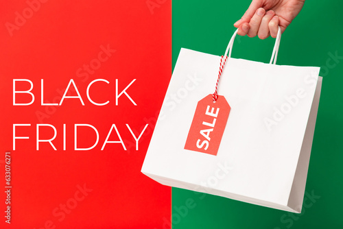 Black Friday sale. Female hand holding two shopping bags with sale price tag on red and green background. Discount, shopping and ecology concept
