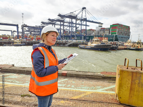 Dock manager on digital tablet infron of huge cargo ship being loaded at port photo