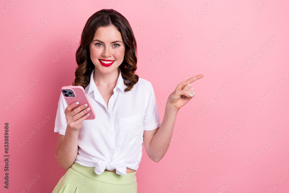 Photo of shiny cute young girl dressed white top typing modern gadget pointing empty space isolated pink color background Photo of shiny cute young girl dressed white top typing modern gadget pointing empty space isolated pink color background