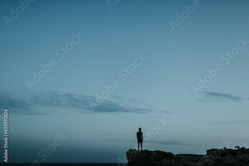 Silhouette of a young man on rocks at Calo des Moro in Mallorca photo