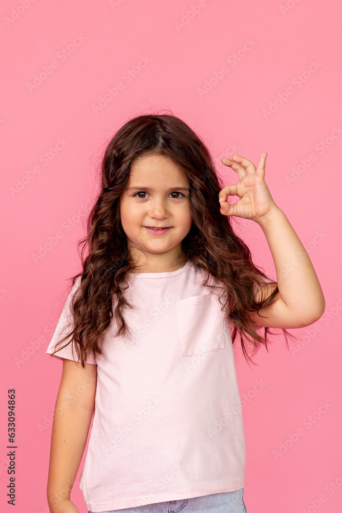 Portrait of young lovely curly hair little child girl show okay symbol advertise promote product on pink color studio background. Mock up. Space for text Portrait of young lovely curly hair little child girl show okay symbol advertise promote product on pink color studio background. Mock up. Space for text