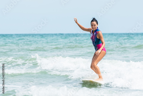 Asian woman standing on a surfboard smiling happy from the surf which is exercise and activities that she enjoys. to people sport and surfboard concept.