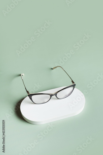 Podium with eyeglasses on pastel green background. Optical store, vision test, stylish glasses concept.