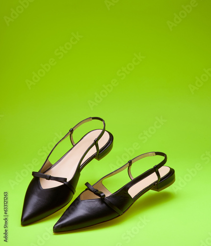 Trendy open-back pointed-toe black women's shoes decorated with bows isolated on a bright green background with copy space. Mock-up for design advertising for a shoe store