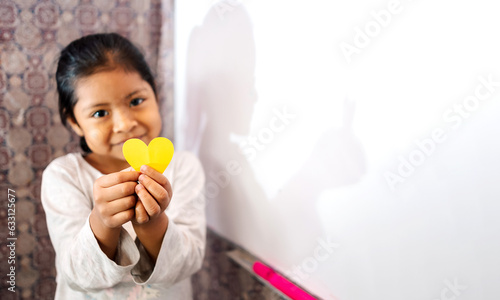 Niña latina sonriente y feliz sosteniendo en sus manos un corazón de papel. Concepto de amor, Esperanza y felicidad. Espacio para texto.