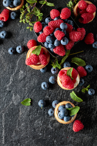 Small tartlets with fresh raspberries and blueberries on a black background Fototapet