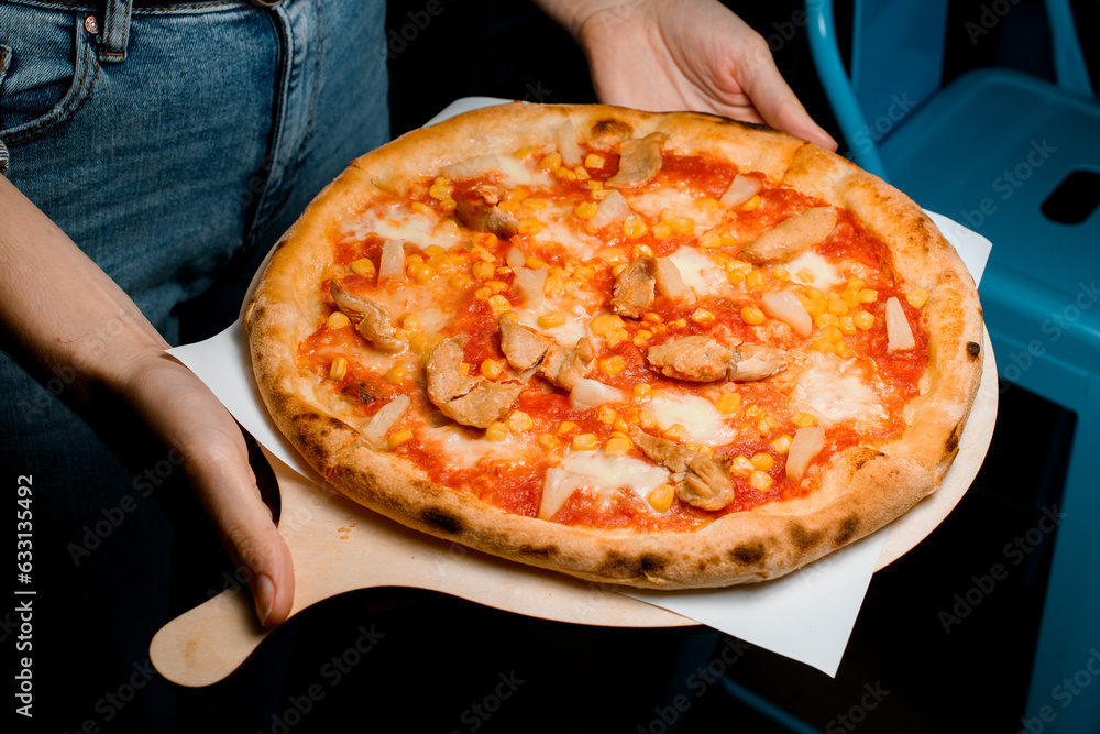 Waitress hold in hands wooden tray with fresh appetizing pizza with crisp crust for guests.