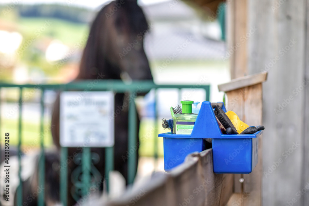 Focus on a horse groom box at a horse barn paddock in summer outdoors. A black horse is seen in the background. Text space - obrazy, fototapety, plakaty 