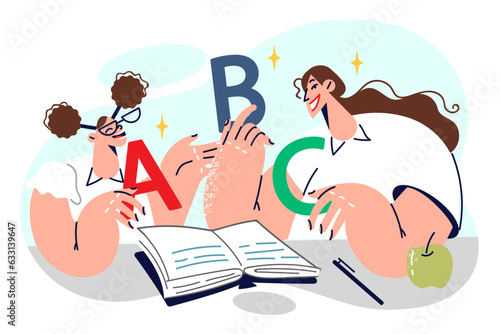 Schoolgirl learns alphabet together with elementary school teacher, sitting in classroom