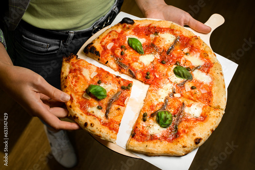 Restaraunt worker hold in hands wooden tray with fresh delicious Italian pizza and separates one slice