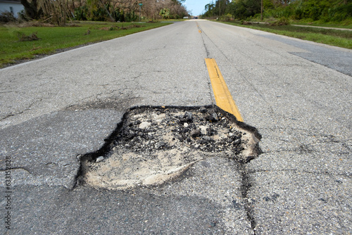 Damaged asphalt road with deep pothole on american highway surface. Ruined roadway in urgent need of repair