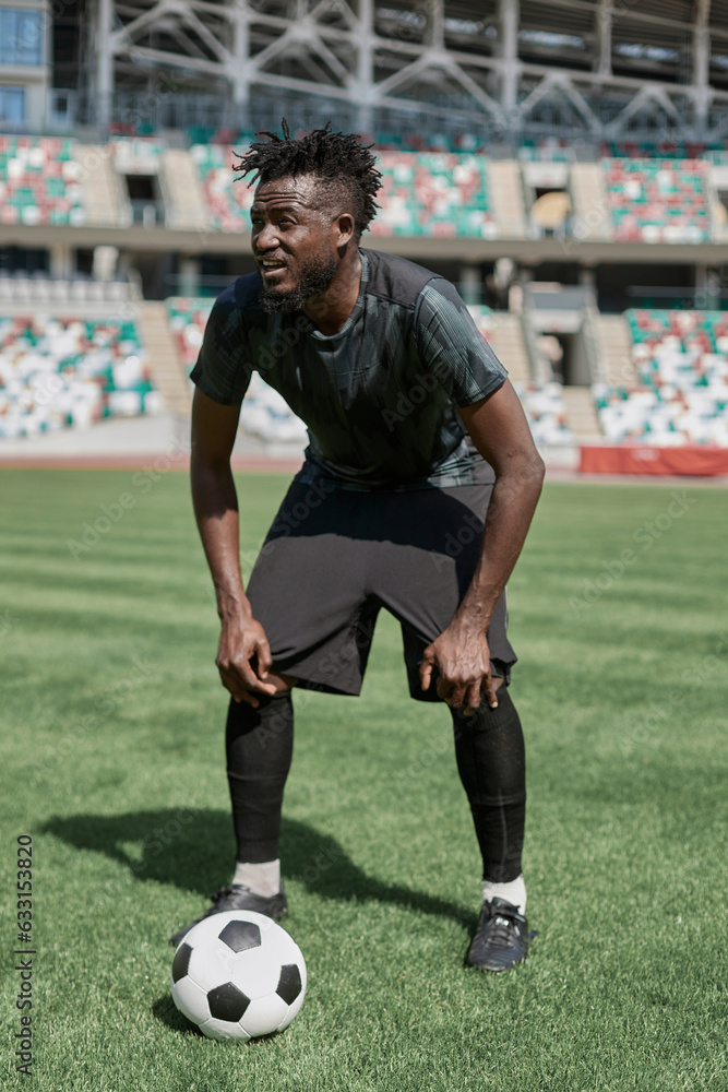 Confident young african american soccer player kicking ball in stadium