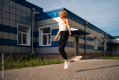 Beautiful blonde woman skipping rope outdoors during workout. Cardio excursuses, healthy active lifestyle. 