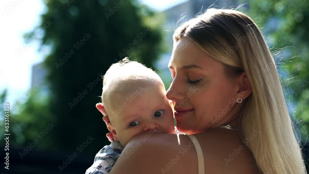 Beautiful blonde woman stands half-back to camera holding a baby. Loving mom caressing her son tenderly. Close up. Beautiful blonde woman stands half-back to camera holding a baby. Loving mom caressing her son tenderly. Close up.