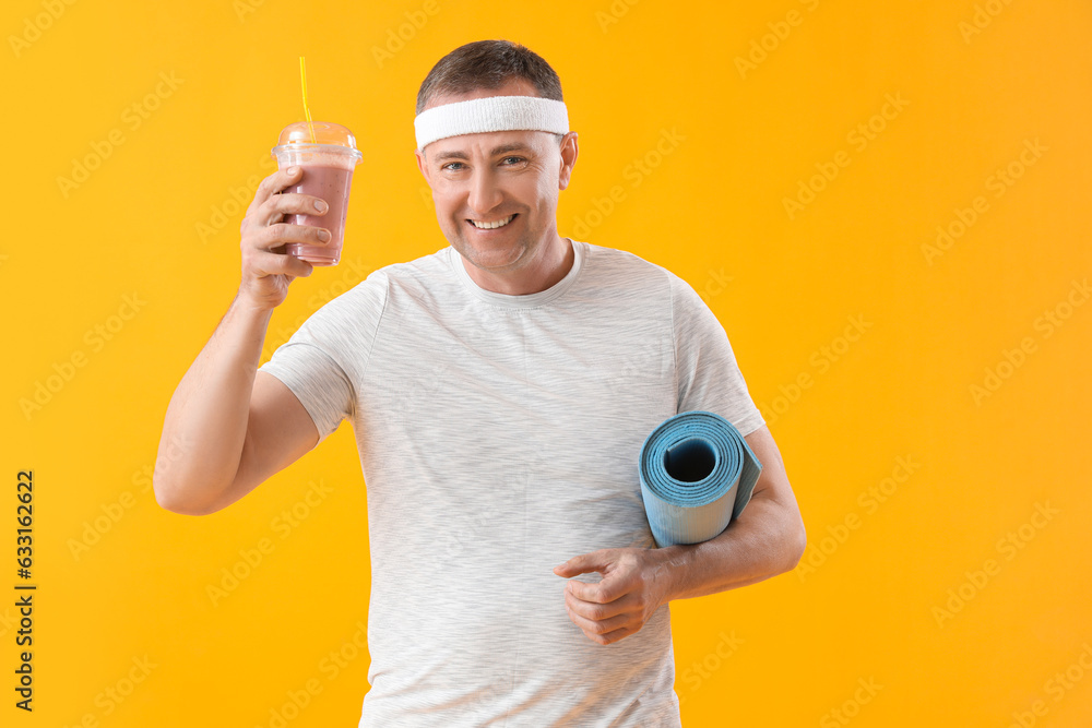Sporty mature man with glass of fruit smoothie and fitness mat on yellow background Sporty mature man with glass of fruit smoothie and fitness mat on yellow background