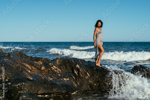 beautiful brunette girl in a silvery net stands on the stones on the seashore © sutulastock