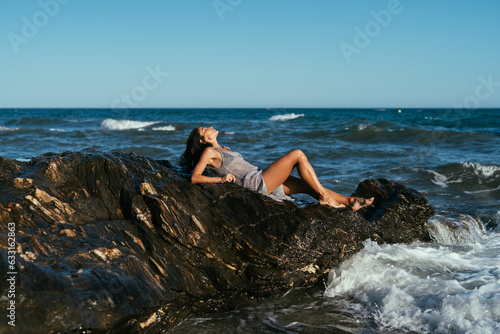 beautiful brunette girl in a silvery net stands on the stones on the seashore