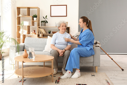 Female caregiver hearing senior woman with stethoscope at home