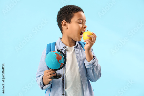 Little African-American schoolboy with globe eating apple on light blue background © Pixel-Shot