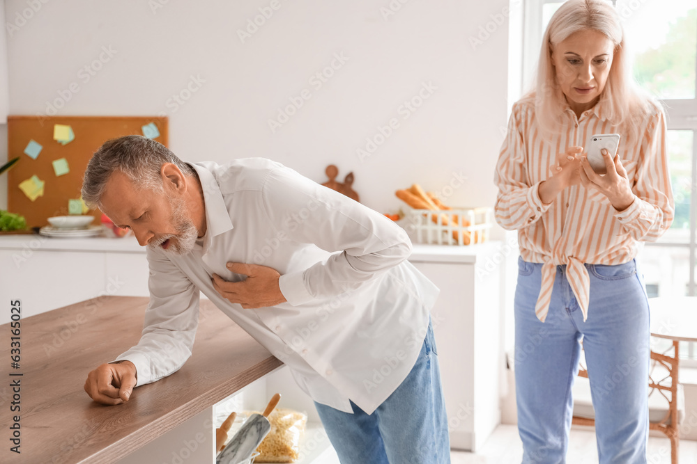 Obraz premium Mature woman and her husband having heart attack in kitchen