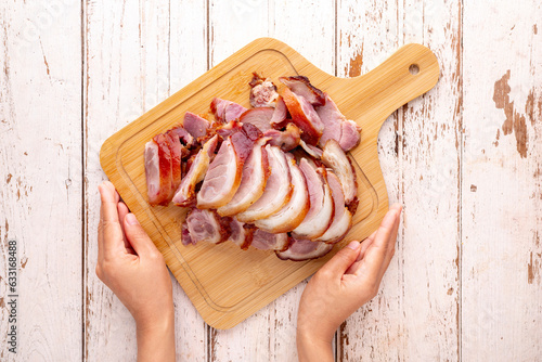 roasted pork knuckle eisbein slice in bamboo wood cutting board served by hands on white wood texture background, top table view, flat lay, German food, pork leg