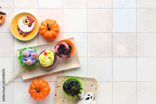 Composition with delicious Halloween cupcakes and pumpkins on light tile background