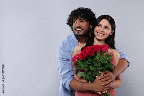 International dating. Happy couple with bouquet of roses on light grey background, space for text