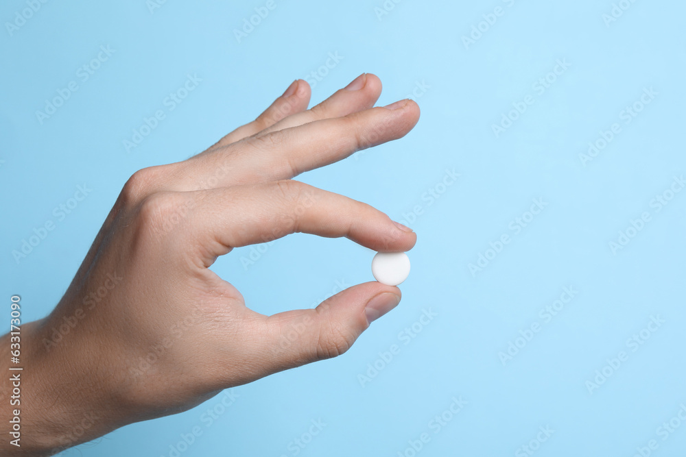 Man holding pill on light blue background, closeup Man holding pill on light blue background, closeup