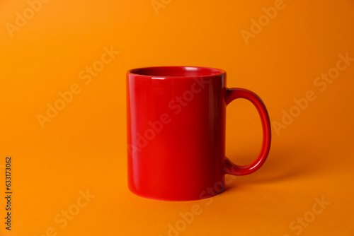 One red ceramic mug on orange background