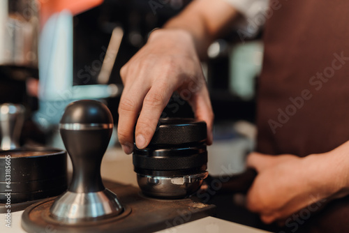 Closeup hand of barista preparation tampering ground coffee in portafilter for espresso machine. Coffee making concept.