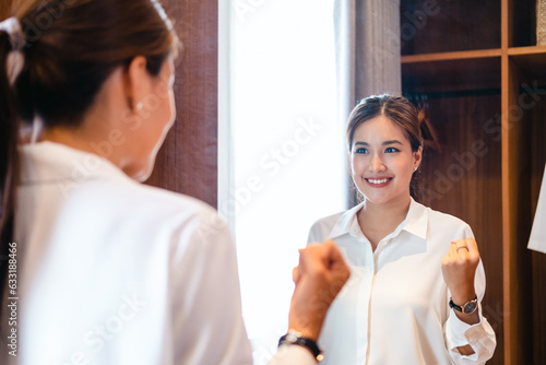 young adult asian self love cheer up pep talk standing looking in mirror before start working. girl get dressed at home before go to work .