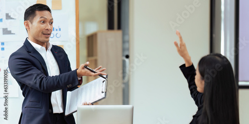Businessman in meeting or seminar pointing towards woman raising hand to say a question.