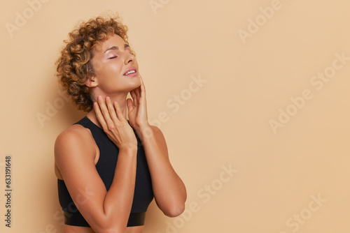 Fotobehang Young curly woman in black bodice stands on light brown background with closed e