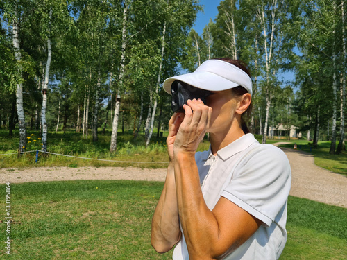 Woman golfer looks into rangefinder to measure distance photo