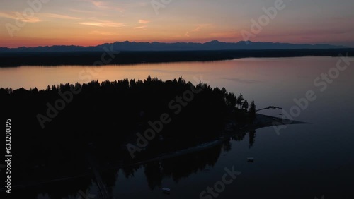 Drone shot of Herron Island's silhouette at sunset with a glowing set of mountains off in the distance. photo