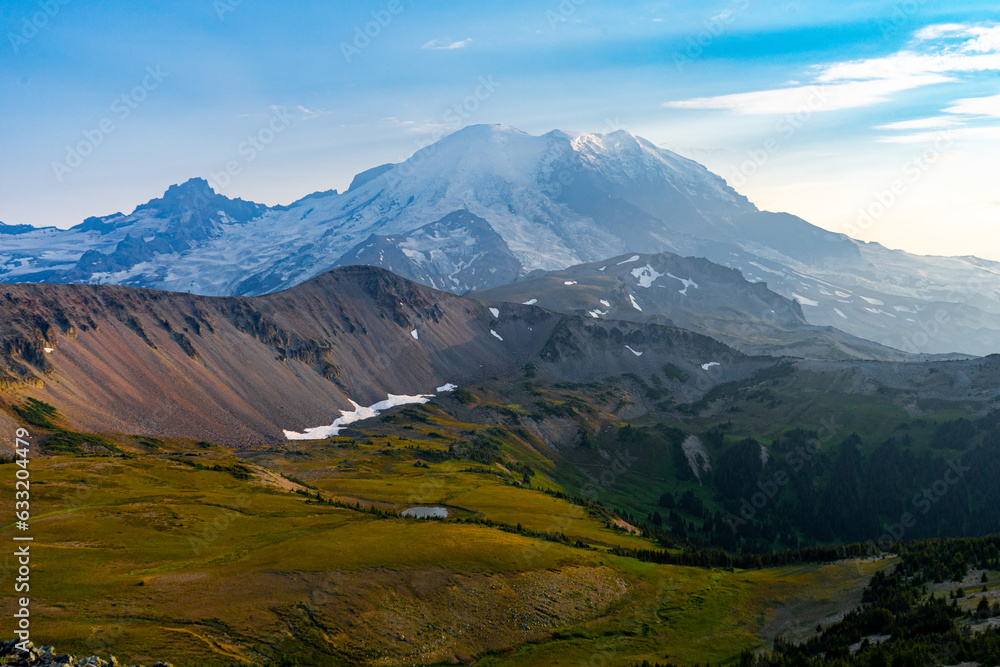 Golden hour view of Mount Rainier with grassy foothills under a blue sky