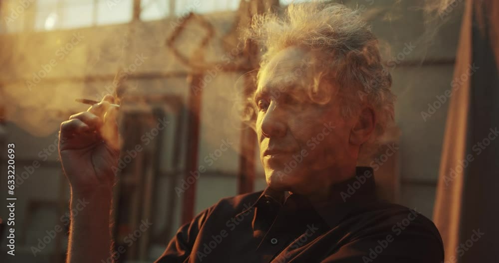 slow motion video of an older man with grey hair smoking a cigarette whilst sitting in his garage after working on his old motorbike. slow motion video of an older man with grey hair smoking a cigarette whilst sitting in his garage after working on his old motorbike.