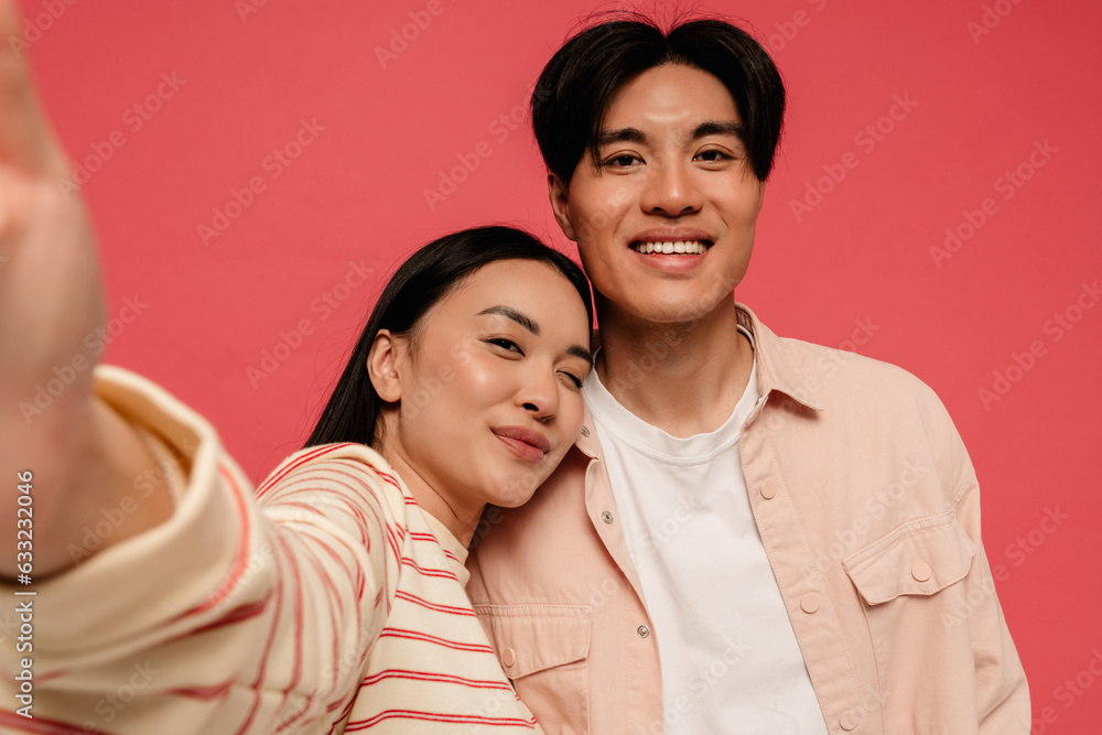 Asian man and woman taking selfie while standing isolated over red background Asian man and woman taking selfie while standing isolated over red background
