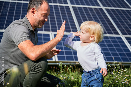 Smiling father and his little child giving each other high-five on background of solar panels. Young father enjoy spending time with his son. Happy family of two on background of solar panels.