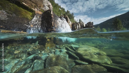 A shallow river with rocky shores and transparent waters, with a waterfall in the background. Over-under water shot. photo