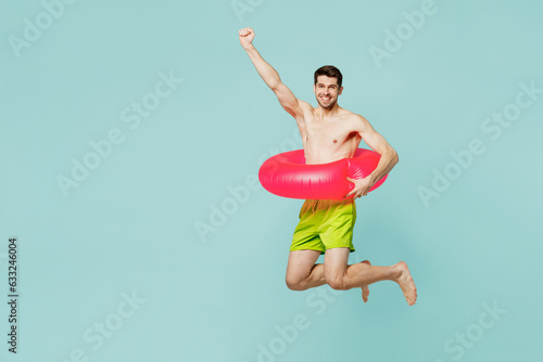 Full body side view young man wear green shorts swimsuit relax near hotel pool jump high in rubber ring do winner gesture isolated on plain blue background. Summer vacation sea rest sun tan concept. photo