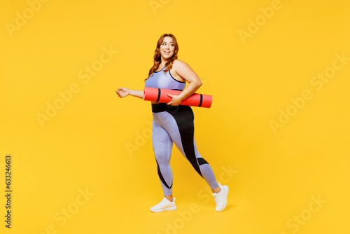 Full body side view young chubby plus size big fat fit woman wear blue top warm up training hold yoga mat look aside on area isolated on plain yellow background studio home gym. Workout sport concept.