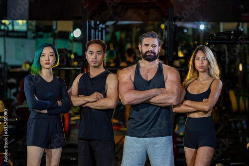 Group portrait of diversity muscular gym trainers standing cross hand together inside gym with dark tone background for exercise and workout concept