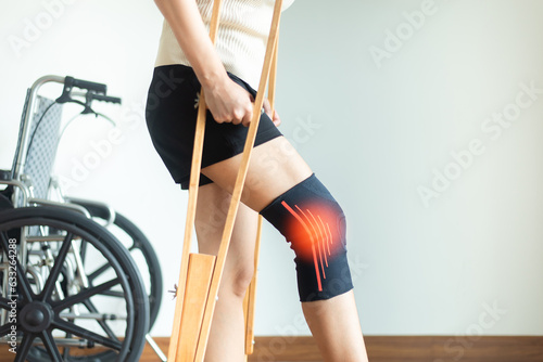 Patient woman using knee support brace and crutches on white background